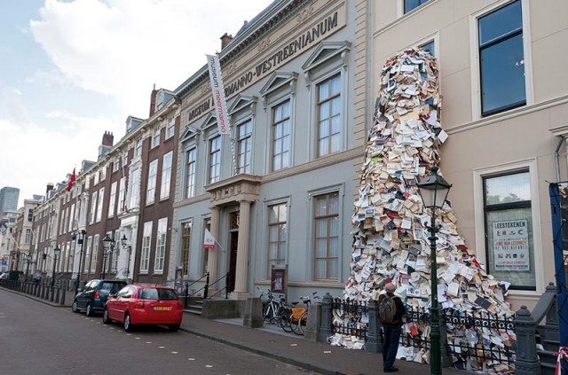 Book sculpture of thousands of books pouring out Museum Meermanno window, by Alicia Martin, contemporary sculpture from Spain
